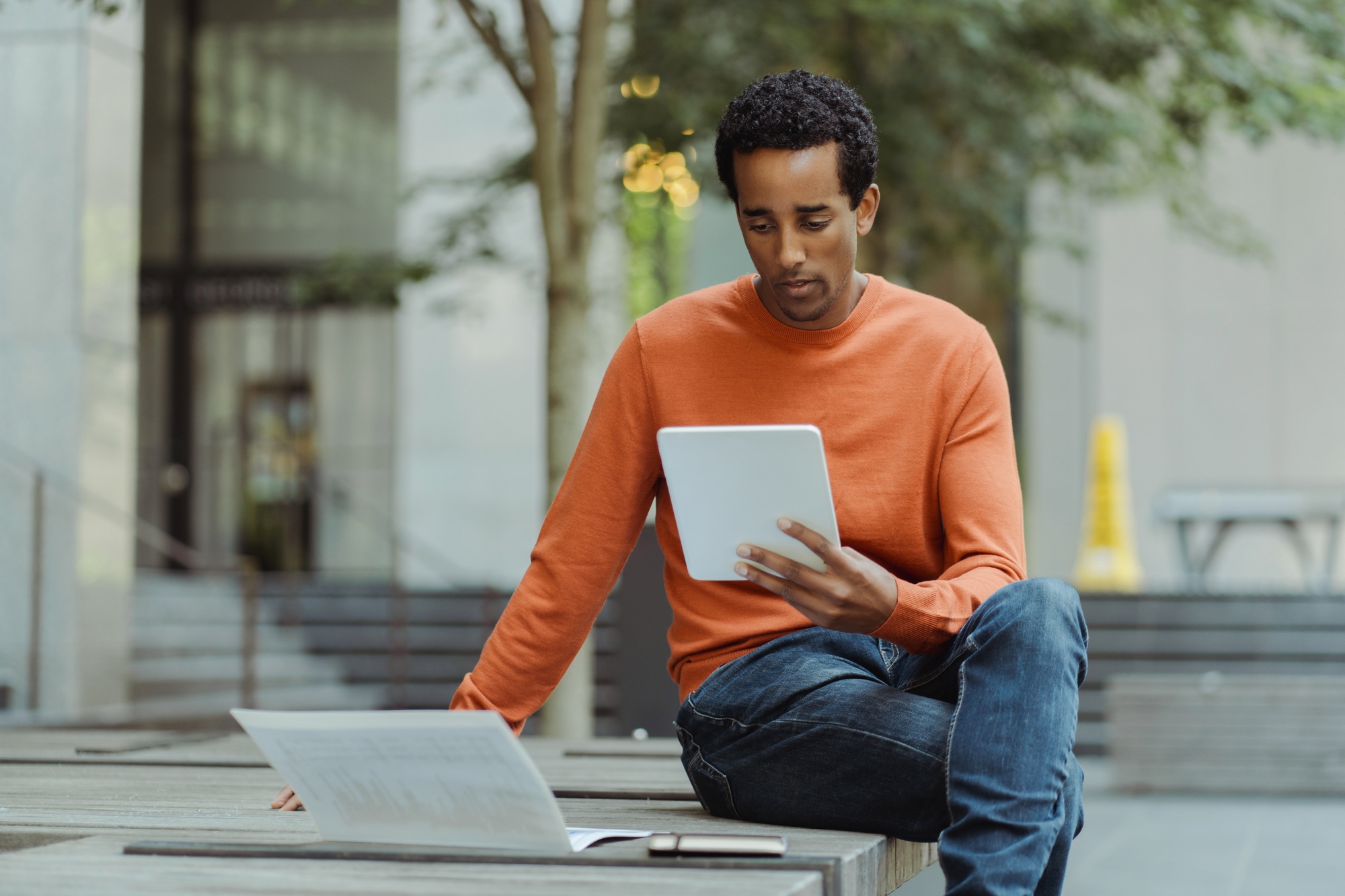 Portrait of African American man holding digital tablet, reading e book, sitting on urban street